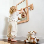 Toddler standing at the wall mounted shatterproof sensory mirror