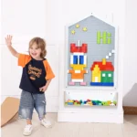 Child standing beside the wall mounted activity board with clear storage box