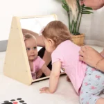 Parent playing with baby in front of the triangular tummy time mirror