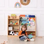 Toddler sitting beside the bookshelf while reading a picture book