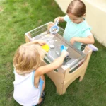 Two children playing at the see-through water and sand table outdoors